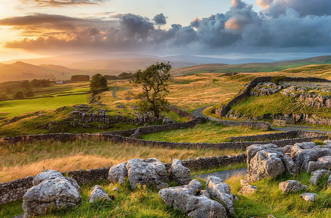 Yorkshire Dales National Park -kansallispuisto muutamine puineen ja kiviröykkiöineen vihreiden nummien keskellä kylpee vielä auringossa synkistä pilvistä huolimatta.